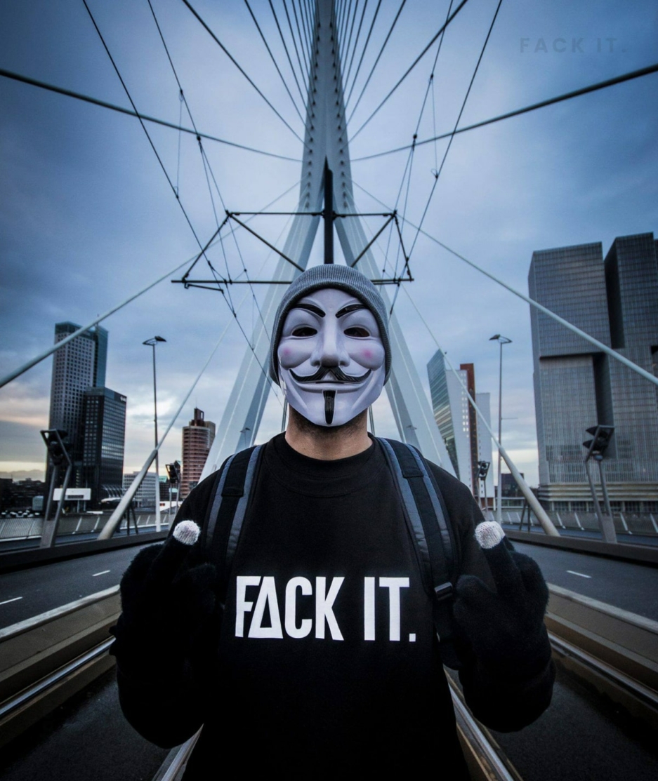 Person wearing an Anonymous mask standing on the Erasmusbrug in Rotterdam, exuding rebellion and mystery with the iconic landmark in the background.