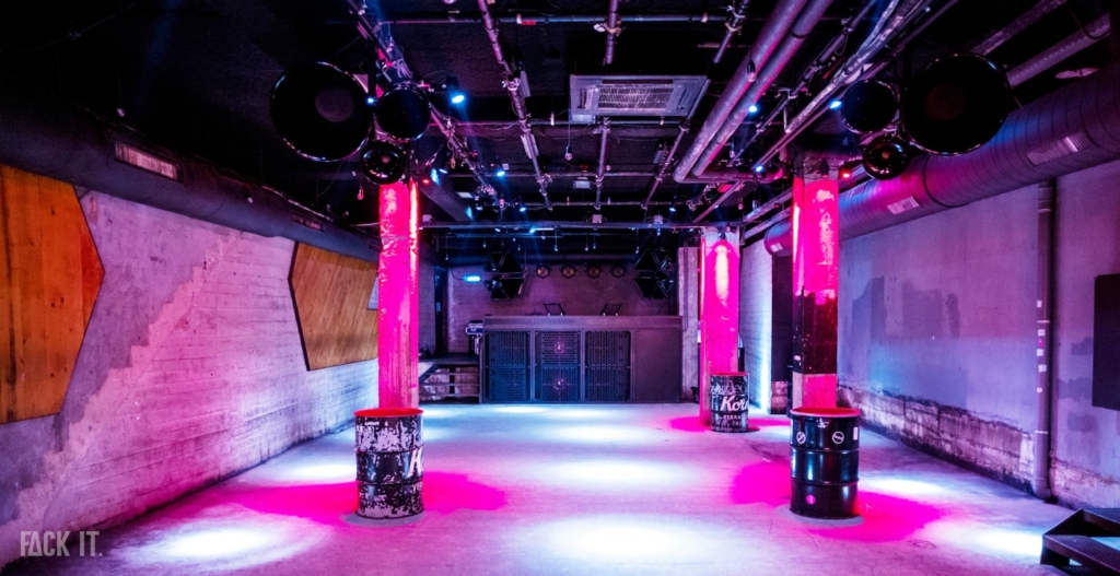 A dark, industrial-style club with high ceilings, exposed brick walls, and a crowd lost in the immersive techno beats.