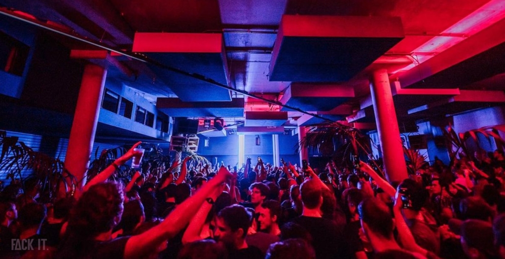 A dark, underground club with a minimalist design, intense strobe lights, and a packed dance floor pulsating to deep techno beats.