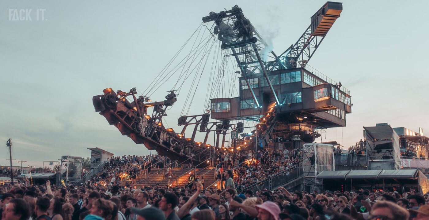 Melt Festival 2025: A vibrant crowd dances at sunset in front of the iconic Ferropolis stage, surrounded by industrial sculptures and stunning lakeside views.