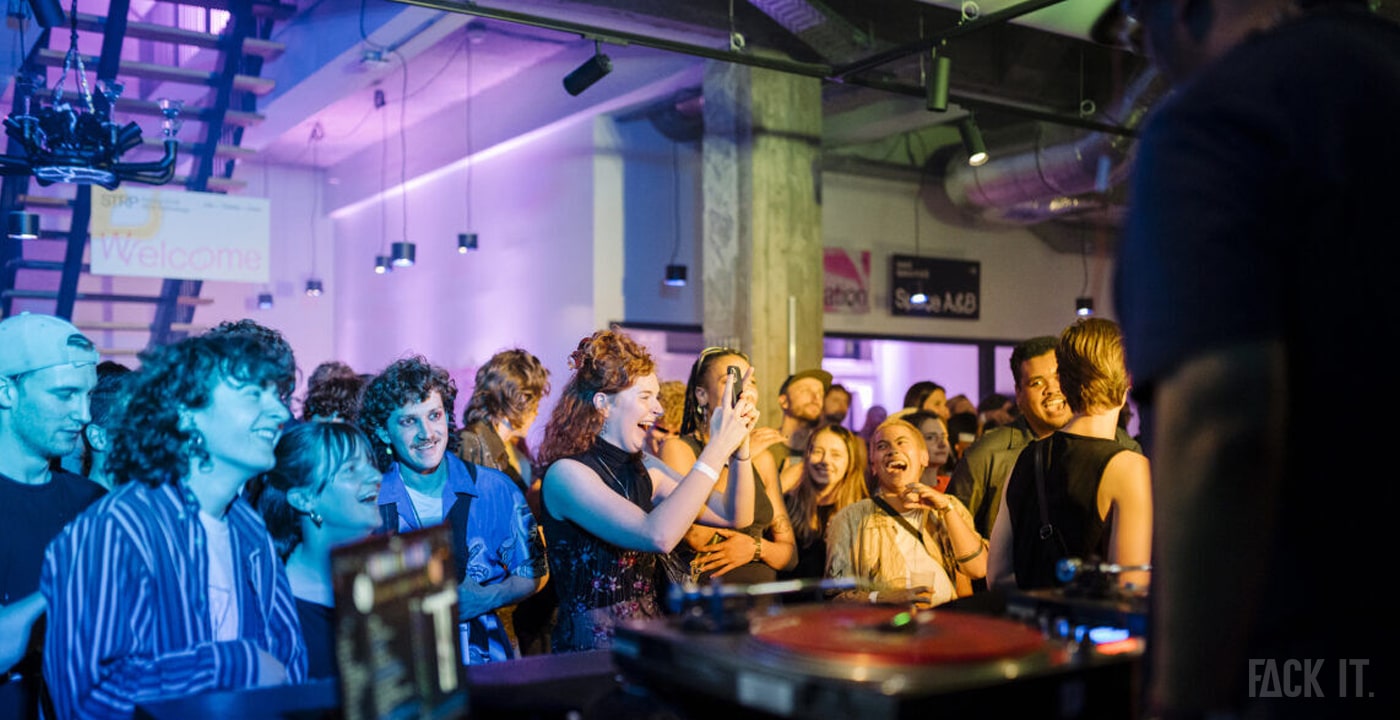 STRP Festival 2025: A joyful crowd dances and laughs at an indoor DJ set, bathed in daylight streaming through large windows, with vibrant visuals and a lively atmosphere.