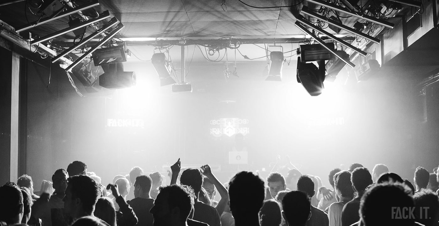 Inside a techno rave 'Fack It' with around 300 people, vibrant lighting illuminating the dancefloor at a club.