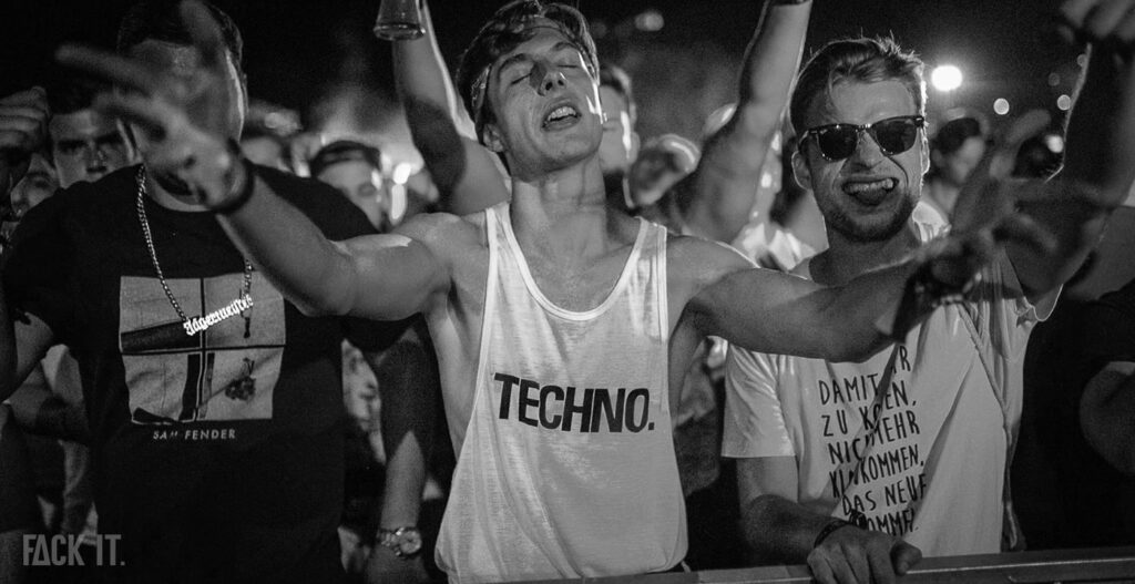 Raver in front of a techno stage with closed eyes, wearing the 'Fack It' Techno tank top, thousands of people in the background.