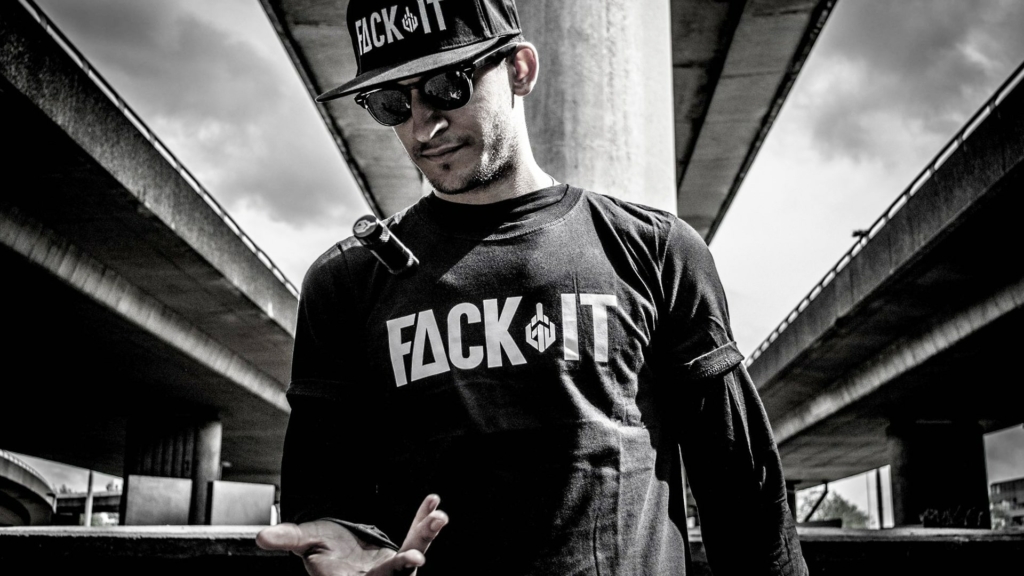 Karim Rave stands confidently under a bridge in Rotterdam, wearing a Fack It t-shirt and stylish shades.