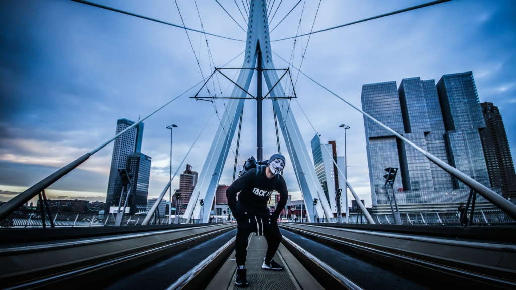 Karim Rave stands boldly on the tram line of the Erasmusbrug in Rotterdam, with the city skyline in the background.