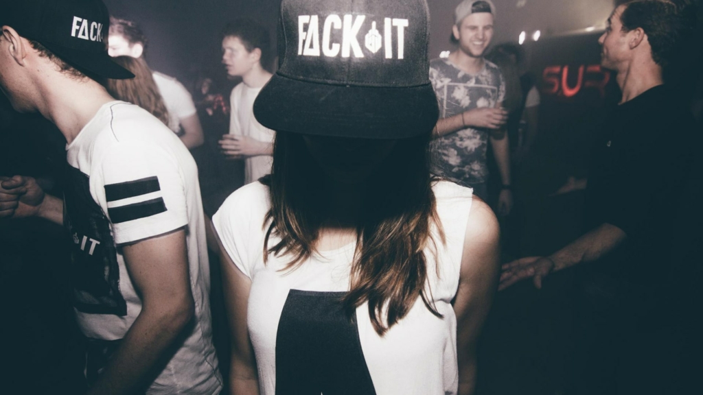 A girl wearing a Fack It snapback, enjoying the night in a vibrant club atmosphere.