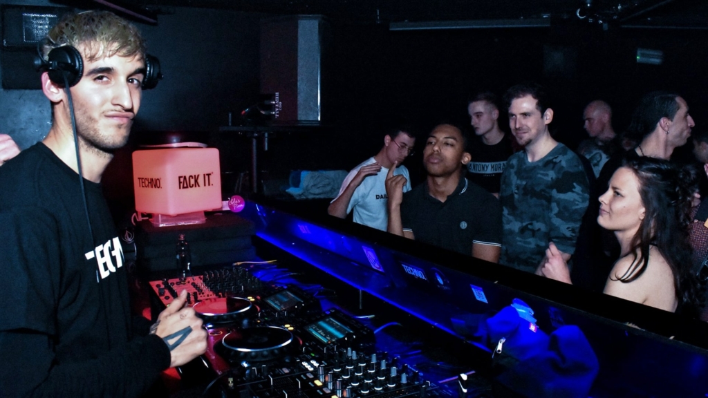 DJ Onedefined stares boldly into the camera while performing at Toffler, the crowd vibing in the background.