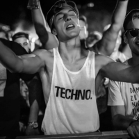 Raver in front of a techno stage with closed eyes, wearing the 'Fack It' Techno tank top, thousands of people in the background.
